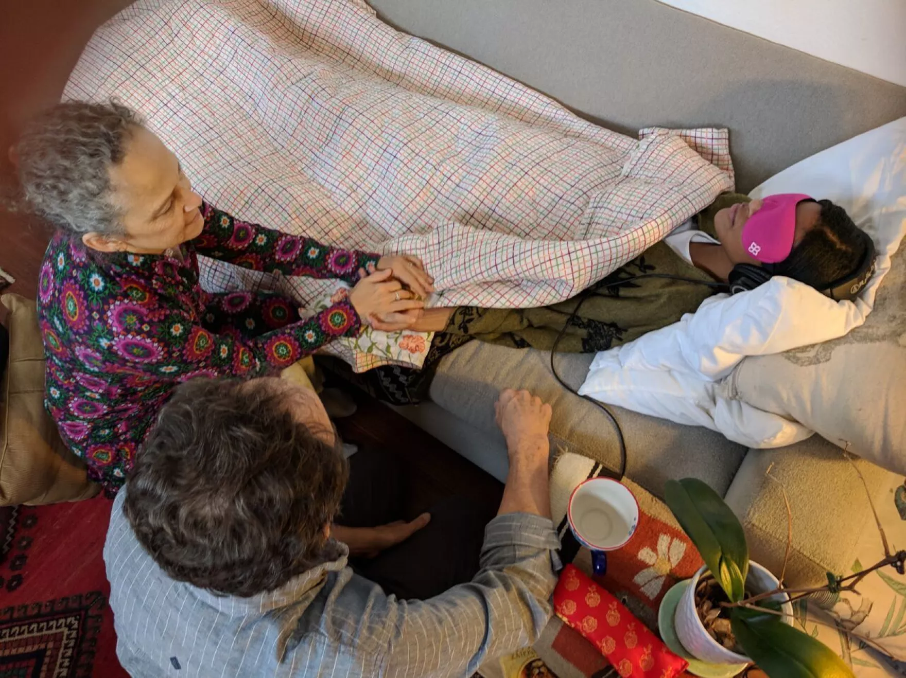 Two therapists sitting with a participant resting with an eye mask during an investigational MDMA-assisted therapy session.